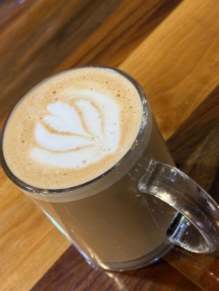 A latte with rosetta latte art in a glass mug on a wooden table.