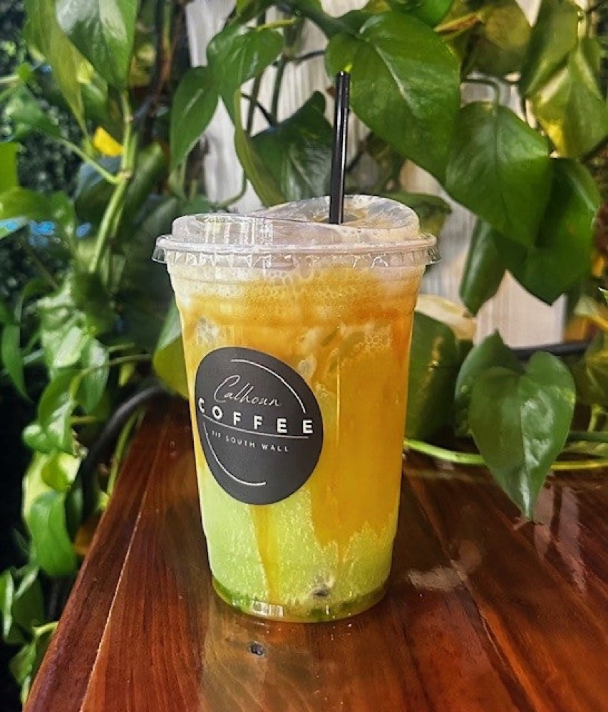 An iced Calhoun Coffee energizer in a branded cup against greenery.