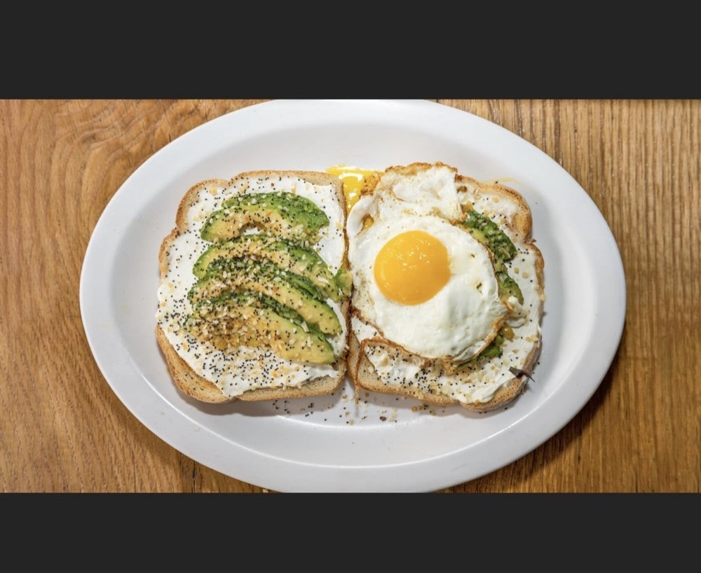 Avocado toast topped with a fried egg on a wooden table.